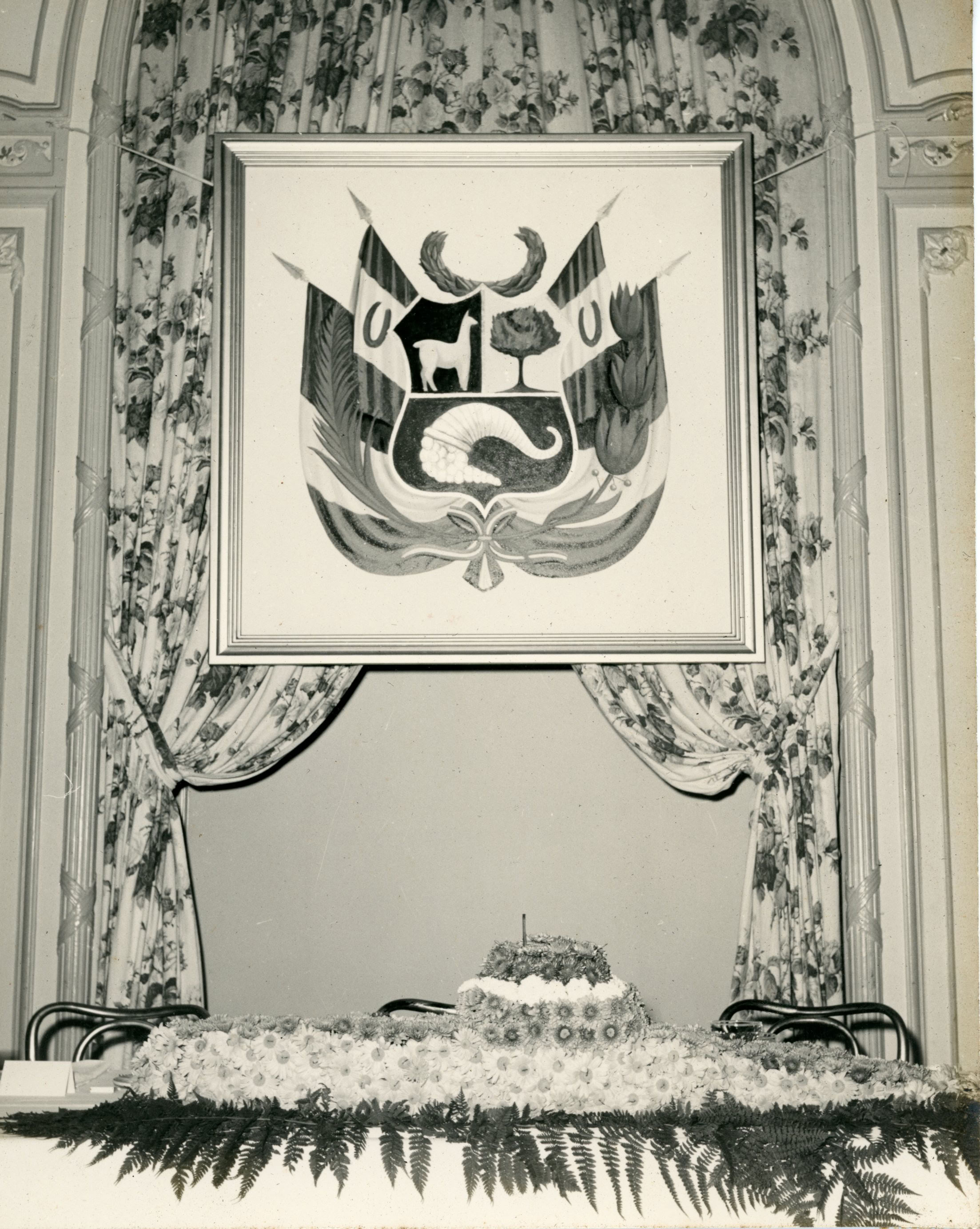 Pastel en forma de submarino, detrás un cuadro con el Escudo Peruano, 1952